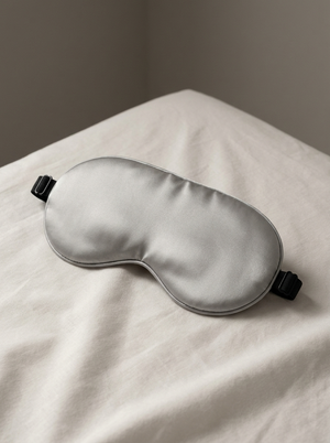 Silensea cooling sleep mask in Cloud Grey resting on a made bed