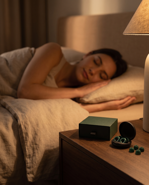 Silensea earplugs and their case on a bedside table, with someone asleep in the background
