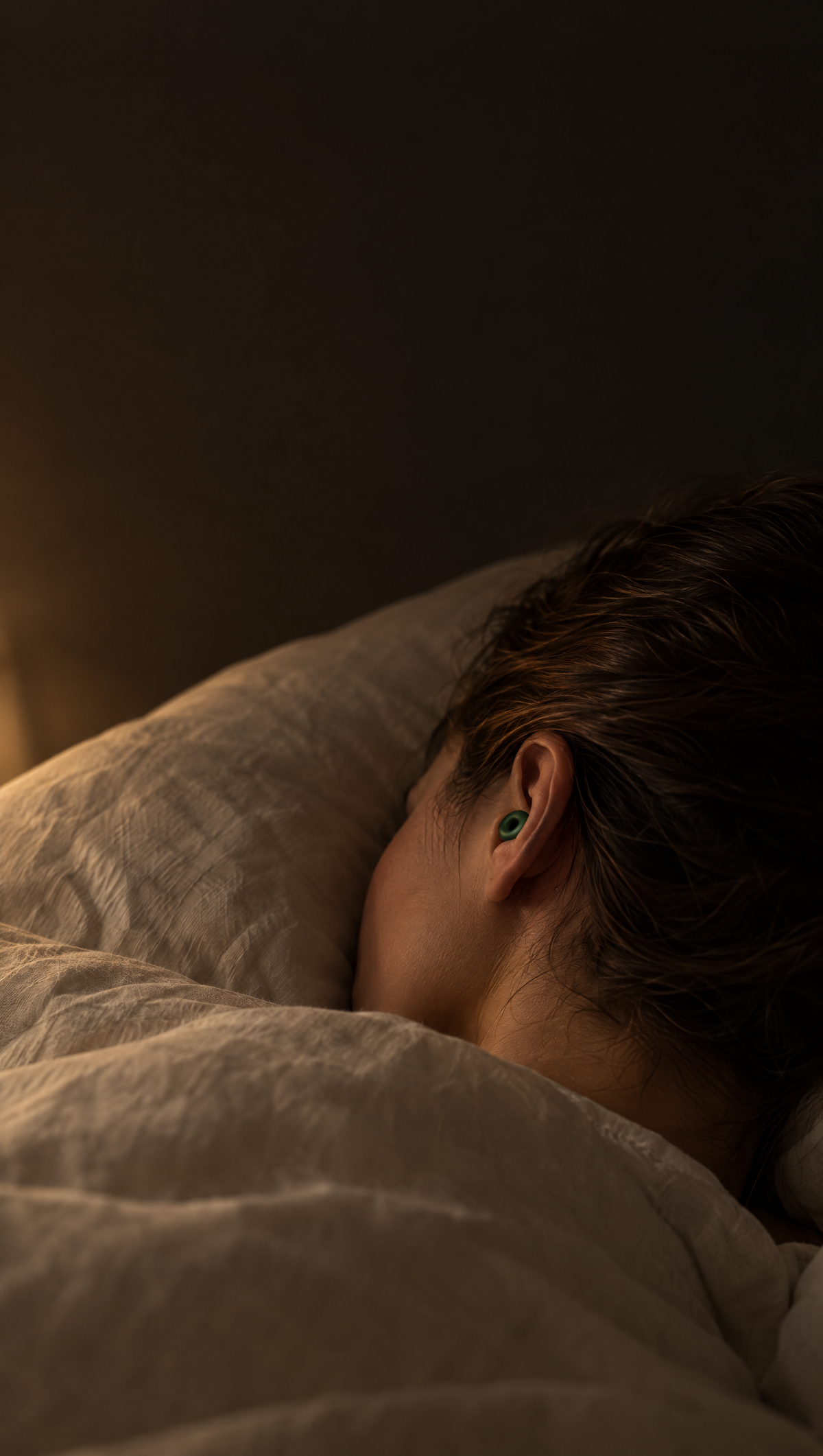 Silensea earplug in Forest Green worn in the ear while sleeping in a dark bedroom