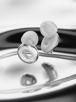 Pair of Silensea earplugs in Moonlight Silver above a liquid metal surface