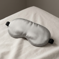 Silensea cooling sleep mask in Cloud Grey resting on a made bed